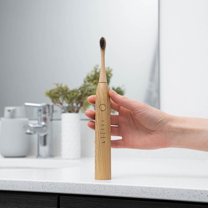 Brosse à dent électrique avec manche en bambou et logo gravé, posée sur un plan de salle de bain minimaliste.

